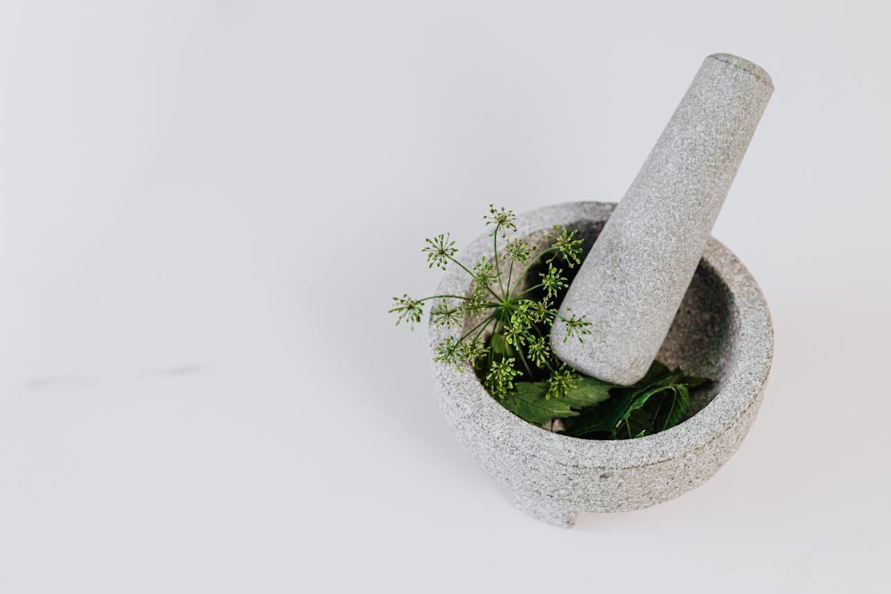 A stone mortar and pestle with fresh green herbs against a white background, perfect for culinary uses.